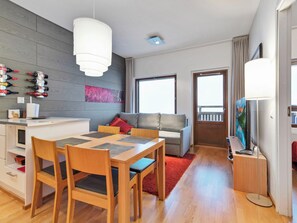 Un espacio habitable moderno con comedor, un sofá, un televisor y una zona de cocina con botellas de vino.