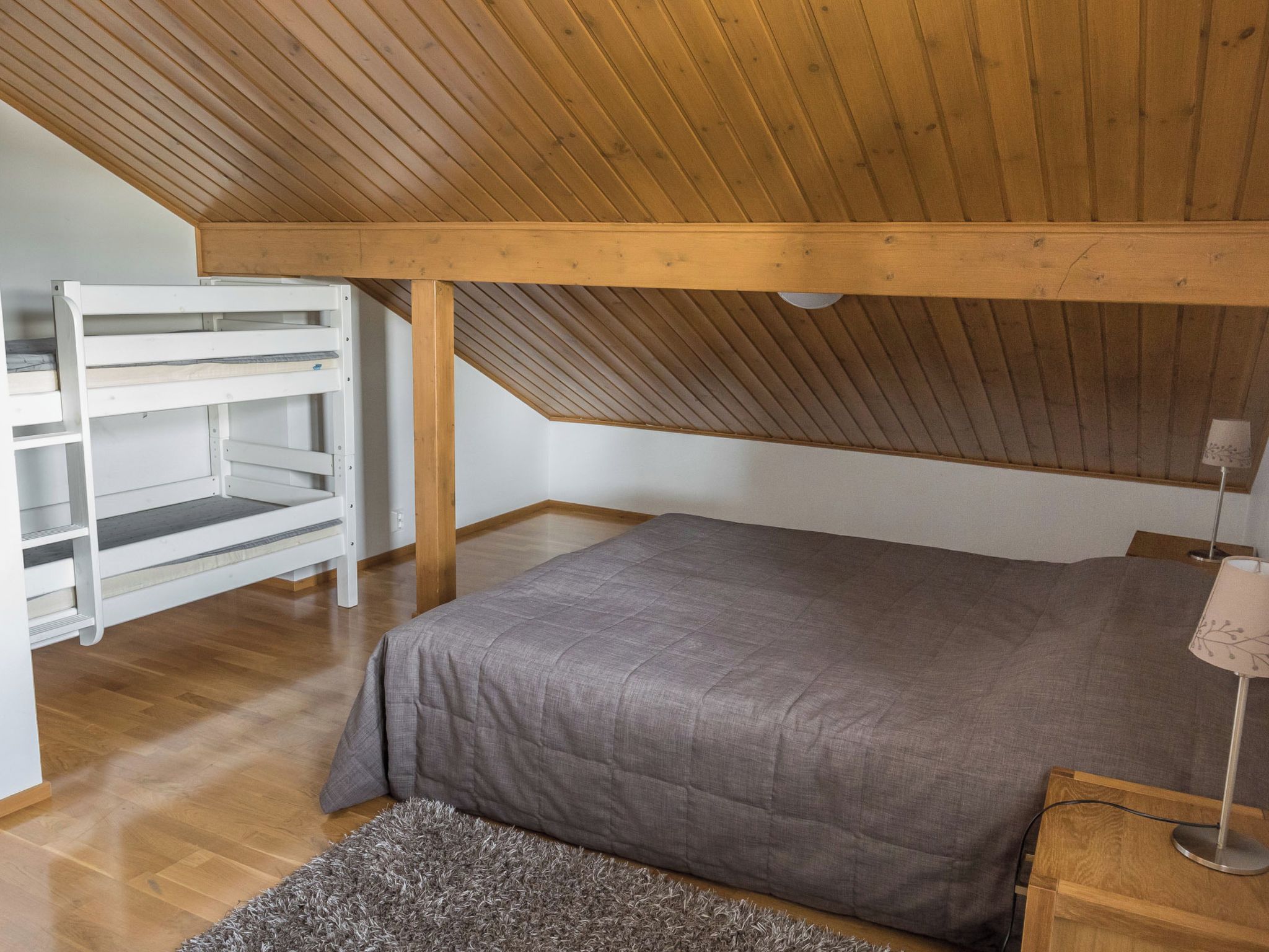 A bedroom with a sloped ceiling, a bed, a nightstand, a lamp, and a built-in shelving unit.