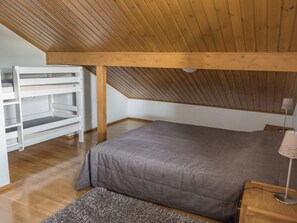 A bedroom with a sloped ceiling, a bed, a nightstand, a lamp, and a built-in shelving unit. - Alppitähti by Interhome (Nilsiä)