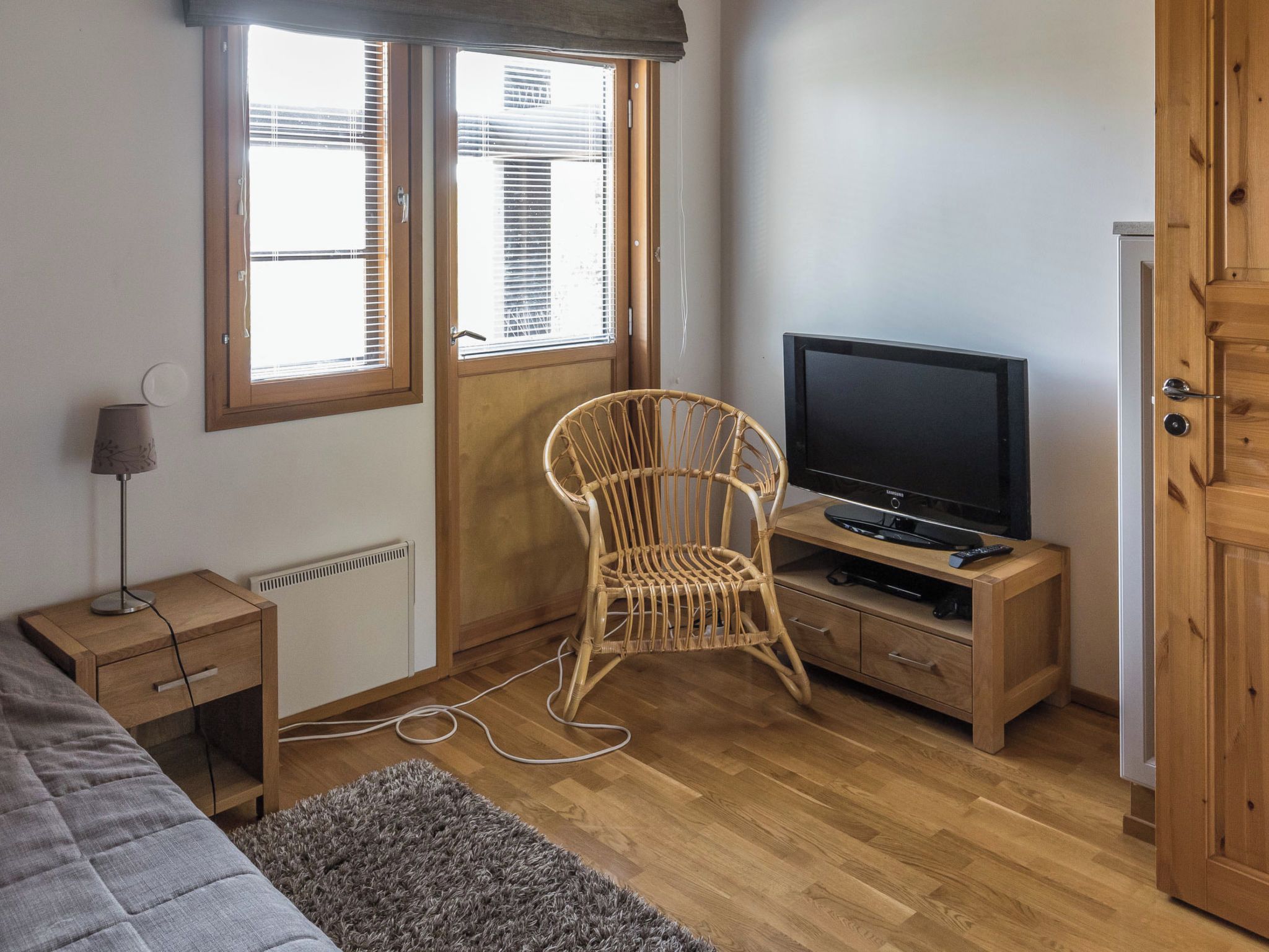 Een slaapkamer met een bed, een stoel, een televisie op een houten standaard, een lamp en een radiator.