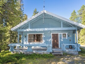 Une petite cabane en bois de couleur bleu clair, avec un toit à pignon, un porche à l’avant et une cheminée.