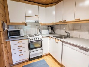 Una cocina compacta con armarios blancos, un microondas, una estufa y un lavaplatos.