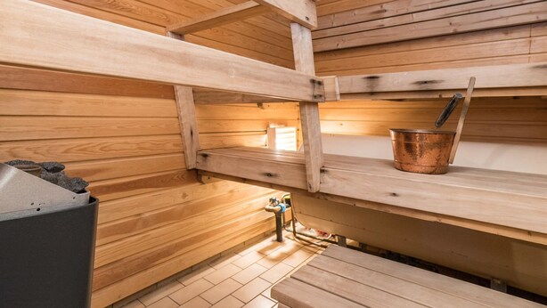 Et sauna-rum med trævægge og bænke, en metalspand og en saunaovn.