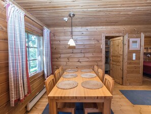 Un interior de madera con una mesa de comedor, sillas, una lámpara colgante y una ventana con cortinas.