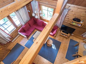 L’intérieur d’une cabine avec un plancher en bois, un canapé rouge, un téléviseur et une fenêtre avec des rideaux.