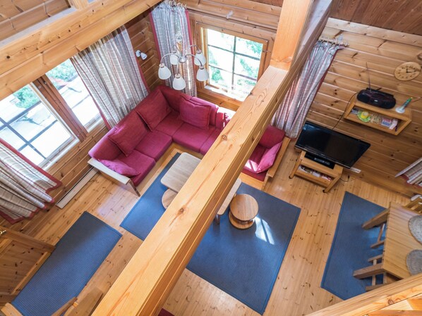 A cabin interior with a wooden floor, a red sofa, a television, and a window with curtains. - Uolevintie 39a by Interhome (Kuusamo)