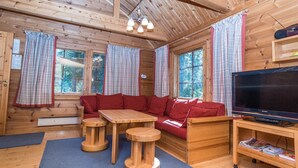 Indbydende interiør i en hytte med træloft, sofa, fjernsyn og bord.