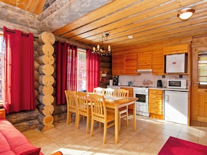 A log cabin interior with a dining area, kitchen, and a stone wall.