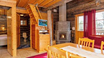 Interior de una cabaña de troncos con una mesa de comedor de madera, sillas, una chimenea y una escalera de madera.