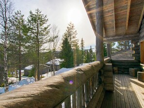 Une terrasse en bois dotée d’une rambarde, qui offre une vue sur un paysage enneigé et boisé.