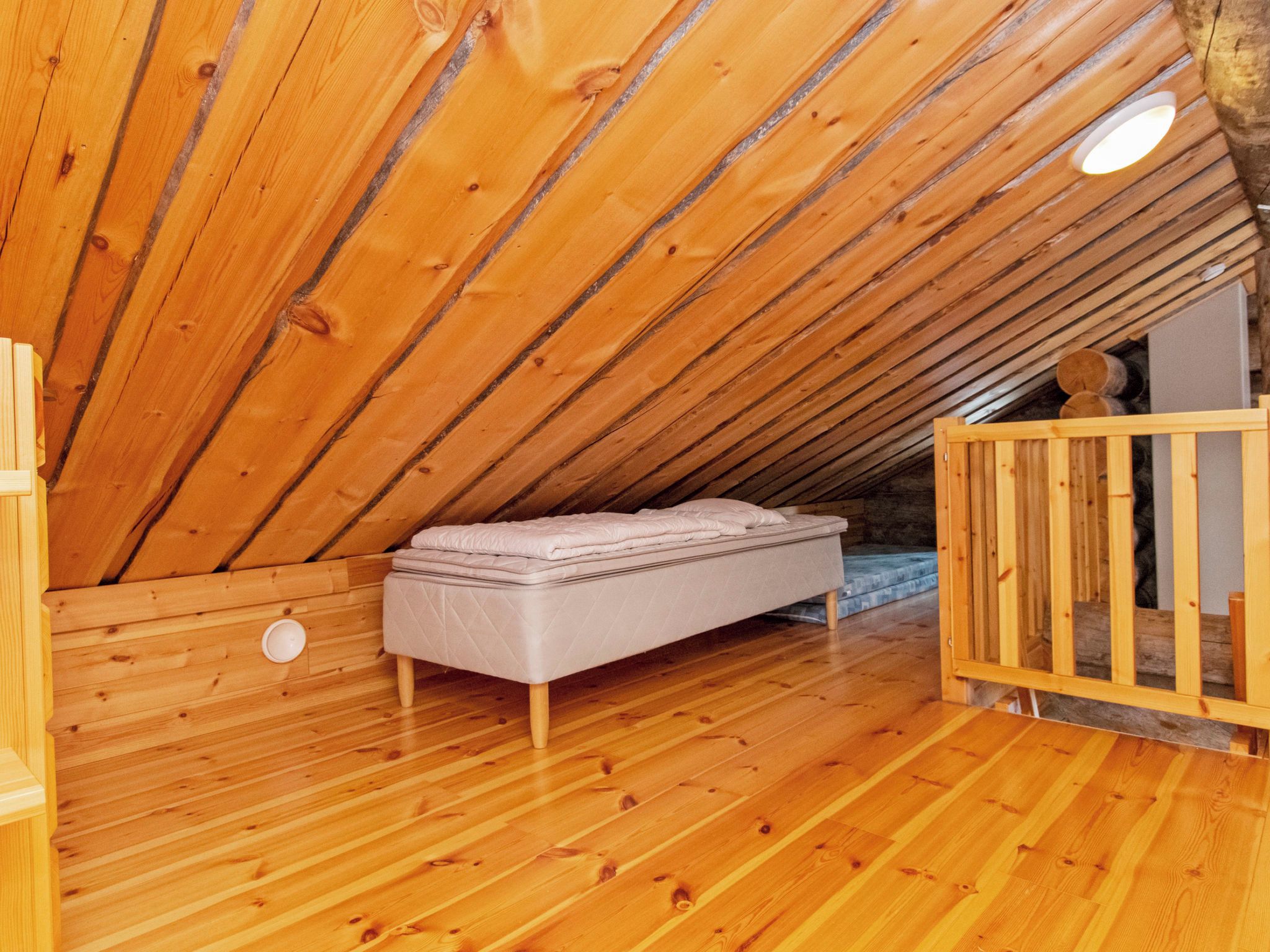 Un interior de madera con techo inclinado, un colchón en el suelo y una cuna.