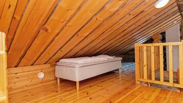 Un interior de madera con techo inclinado, un colchón en el suelo y una cuna.