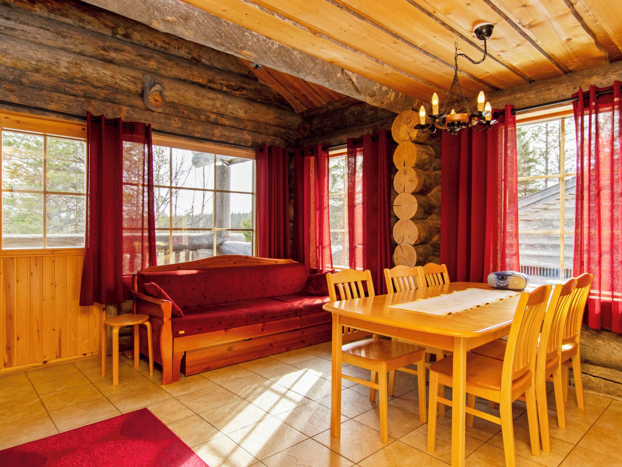 A cozy cabin interior with a wooden dining table, red curtains, and a log wall.