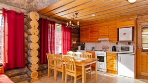 Interior acogedor de una cabaña con una mesa de comedor de madera, sillas, una cocina con electrodomésticos blancos y una pared de piedra.
