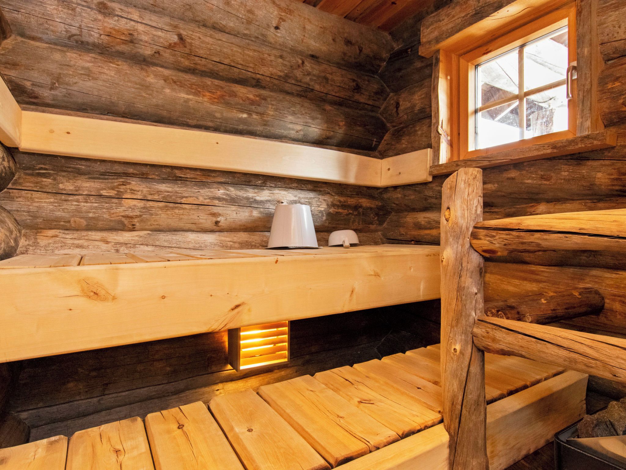 A log cabin interior with a wooden bench, a window, and a small table.