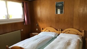 A wooden-framed bed with white bedding in a room with wooden walls and a window with curtains. - Apartment Adler by Interhome (Saas-Fee)