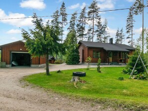 A two-story building with a garage, surrounded by a grassy yard and tall trees. - Vacation home 7152 by Interhome (Sulkava)