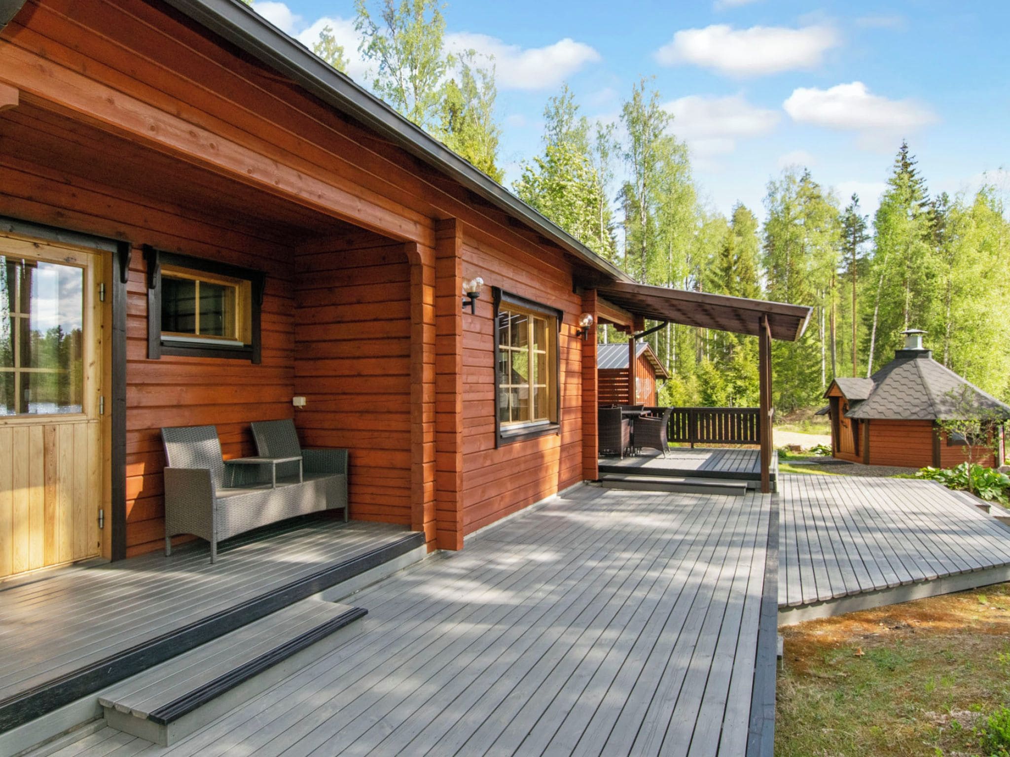 A wooden cabin with a deck, outdoor seating, and a small shed.