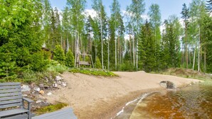 Eine Holzterrasse mit einer Bank, ein sandiger Strand und ein bewaldetes Gebiet mit einer Schaukel.