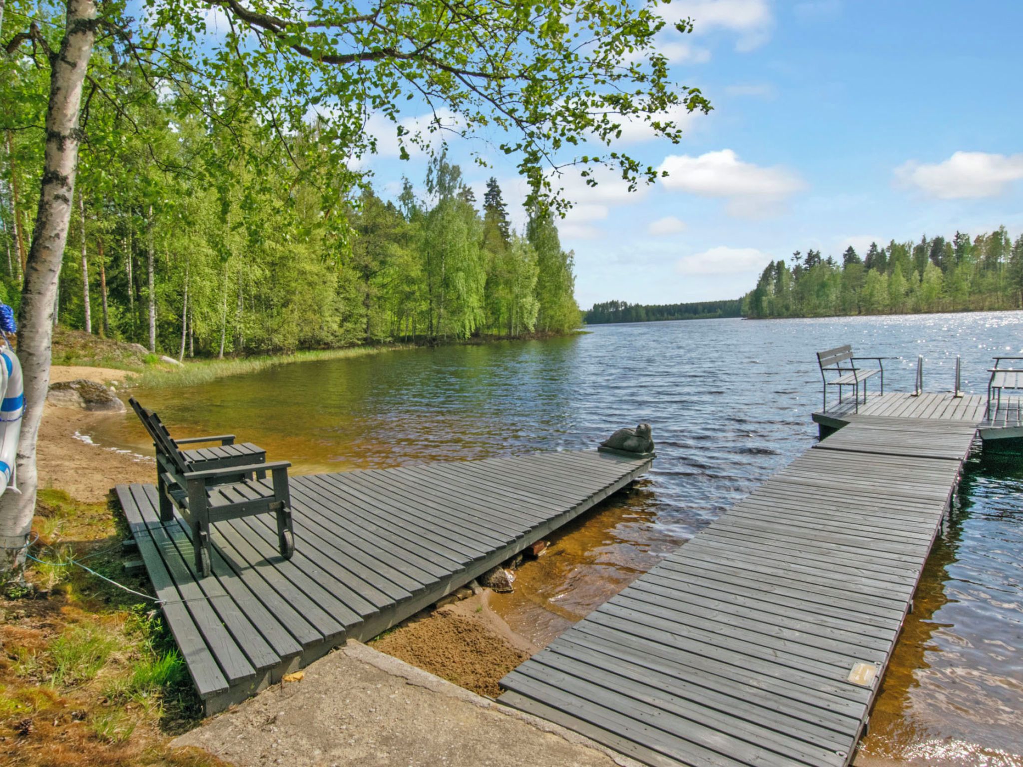 A wooden dock extending into a calm lake, surrounded by dense green trees.