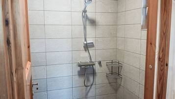 A small, tiled shower area with a handheld showerhead and a wall-mounted faucet.
