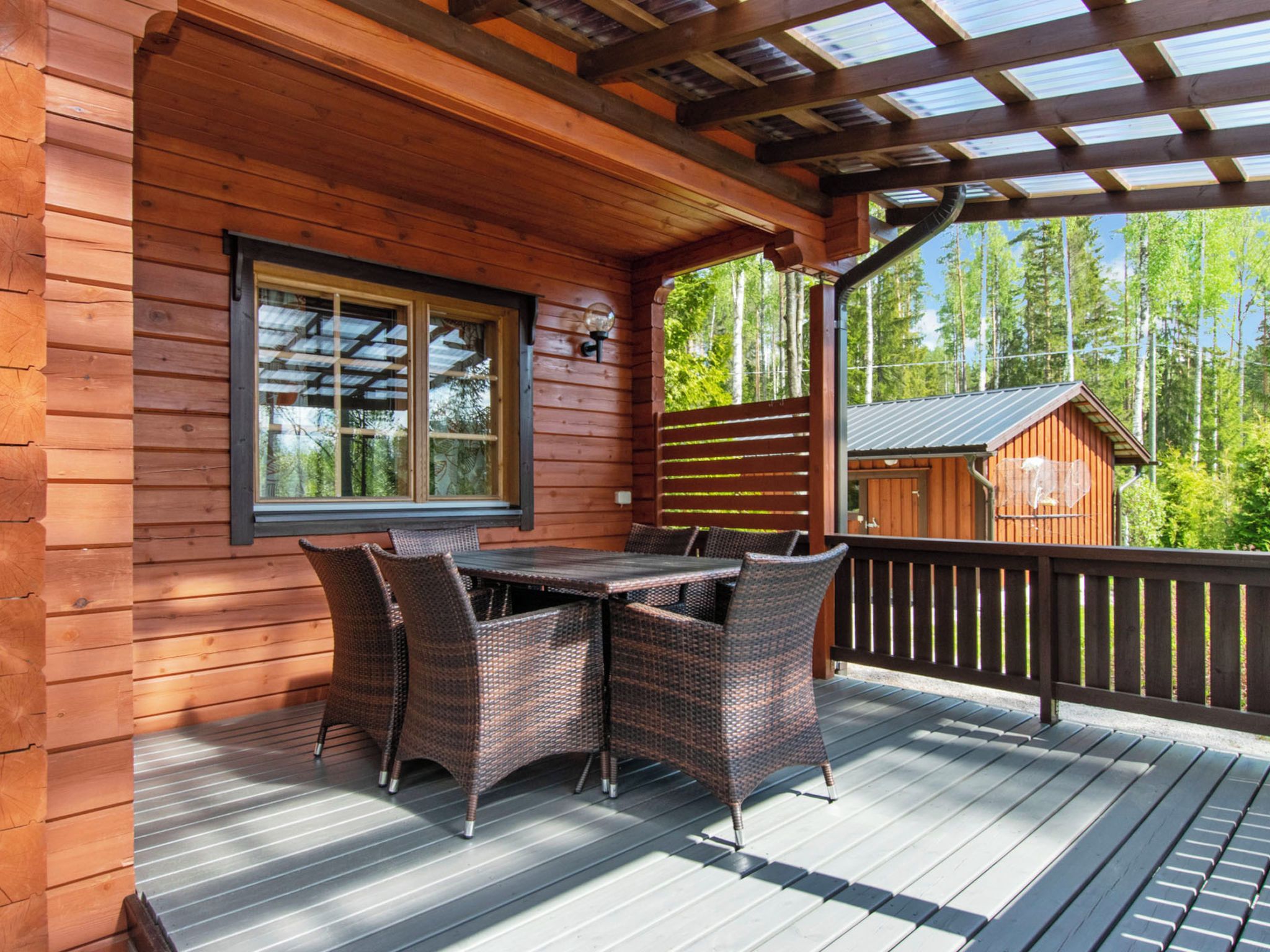 A wooden deck with a table and chairs, a window, and a view of trees.