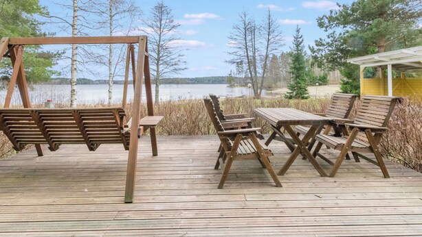 A wooden deck with a swing set and picnic table overlooking a lake.