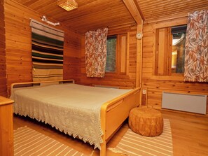 A wooden cabin bedroom with a bed, a window with curtains, a radiator, and a wooden bench.