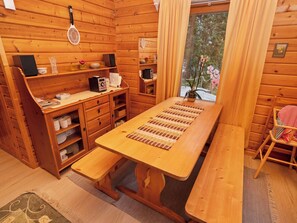 A wooden cabin interior with a dining table, benches, a kitchen area, and a window with a view of trees. - Vacation home Kivelä by Interhome (Kuusamo)