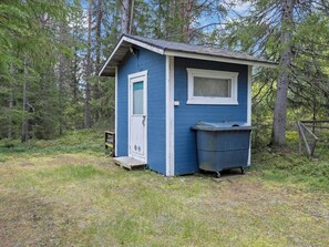 A small blue cabin with a door and window, situated in a wooded area.
