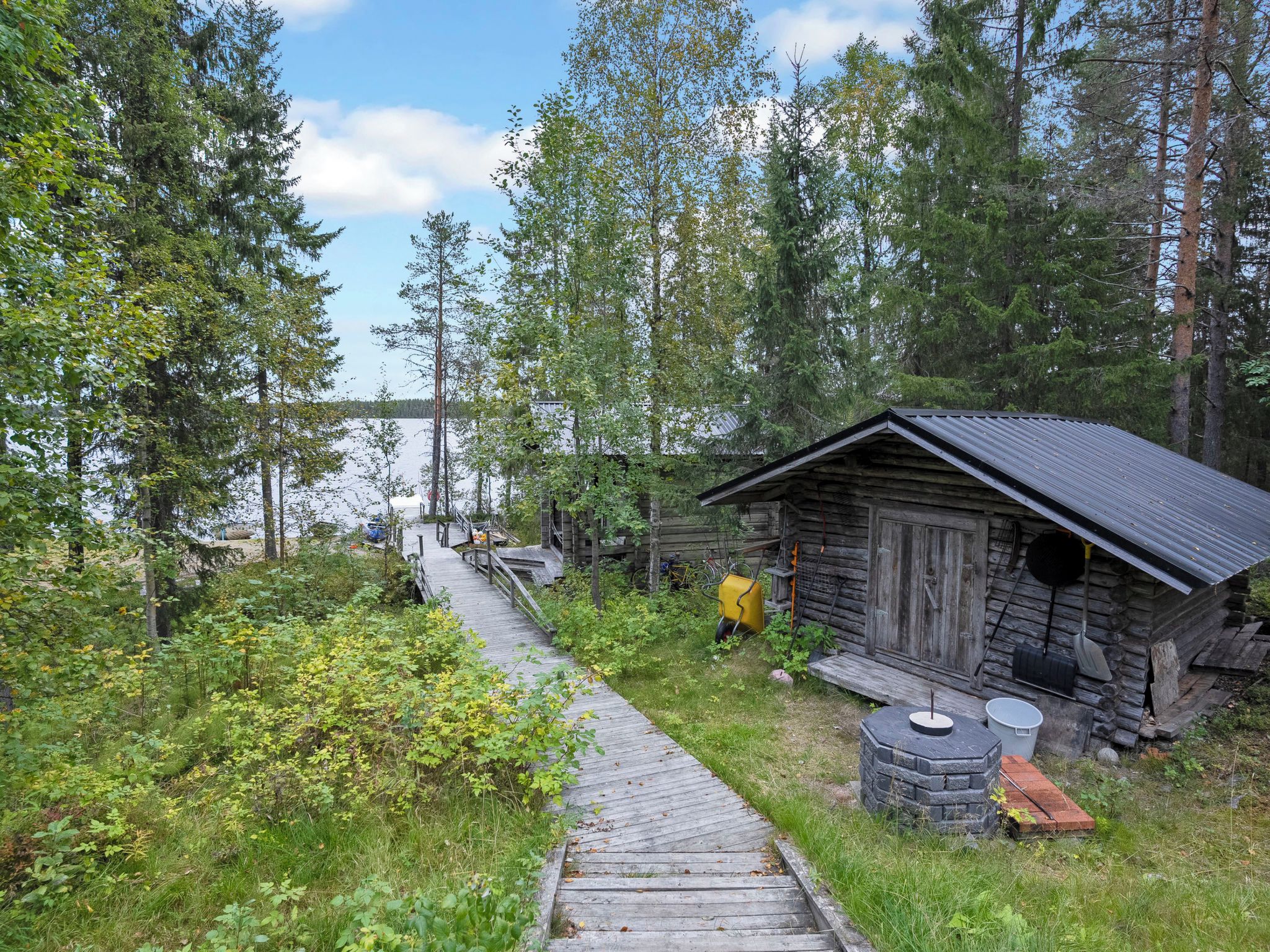 Une cabane en bois, surmontée d’un toit en métal, entourée d’une forêt dense et sous un ciel dégagé.
