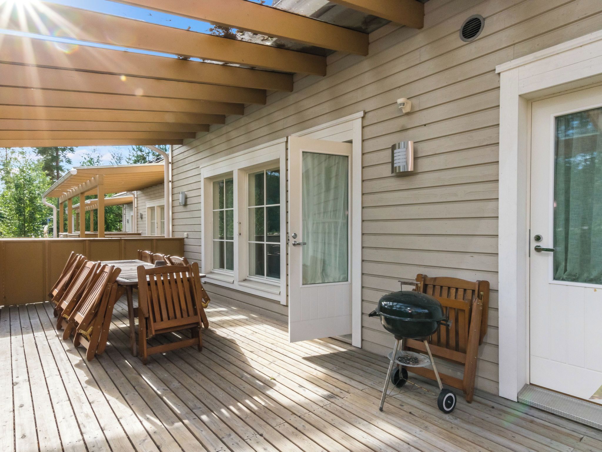 A covered deck with wooden furniture and a grill.
