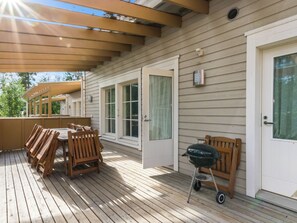 Une terrasse couverte, aménagée avec des meubles en bois et dotée d’un barbecue.