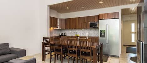 A modern kitchen with wooden cabinets, a stainless steel refrigerator, and a dining area with a table and chairs.