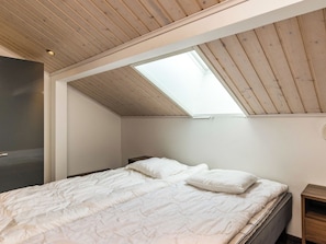 A bedroom with a sloped ceiling, a skylight, a bed with white bedding, and a nightstand.
