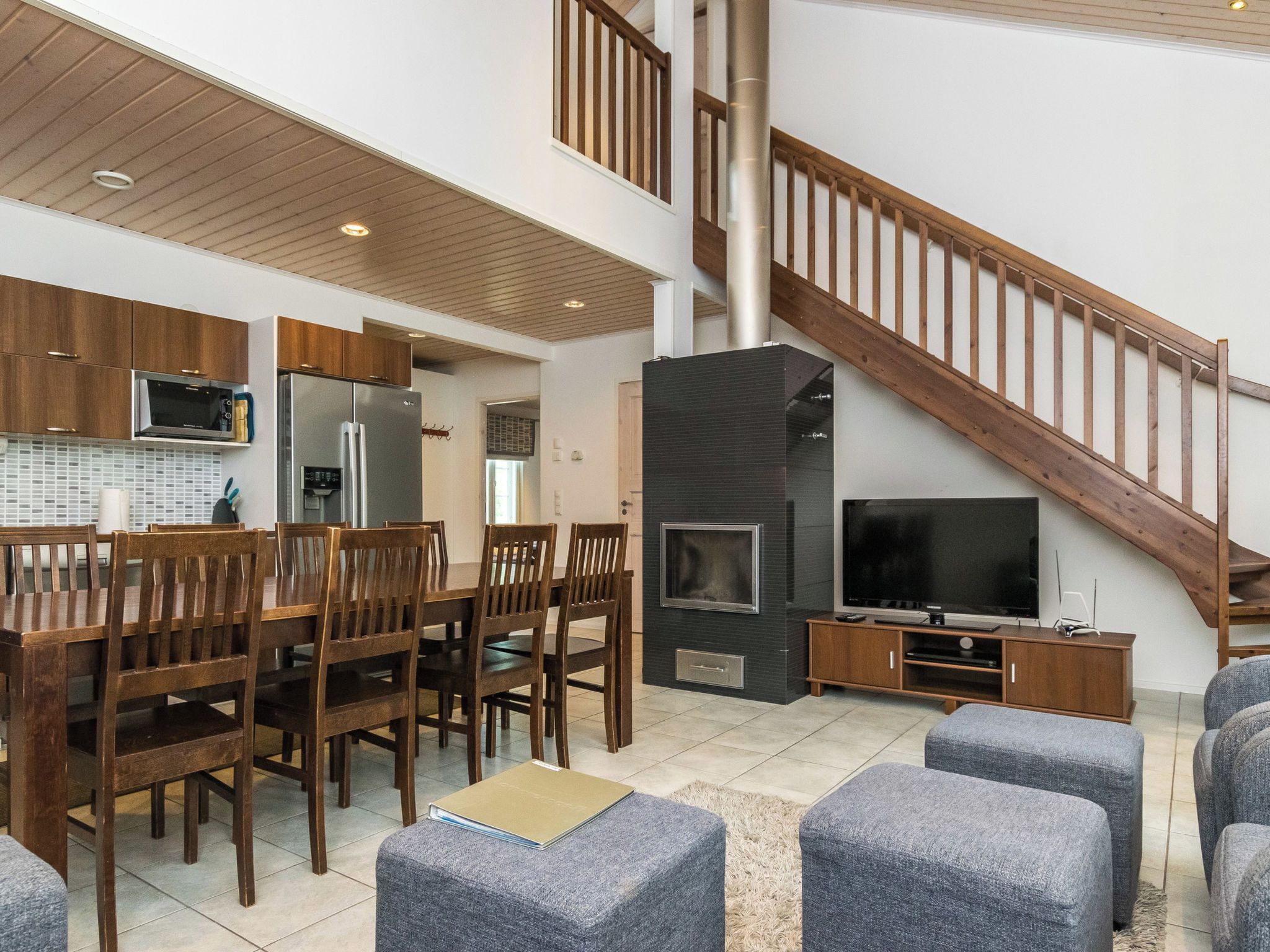 A modern living room with a dining area, a fireplace, a TV, and a staircase.
