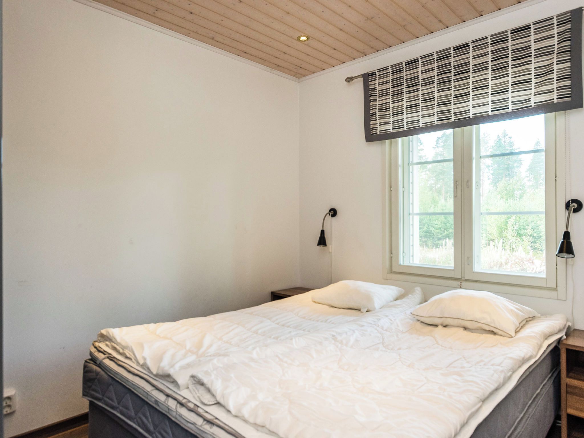Quarto com cama, janela com persianas, abajur e luminária na parede.
