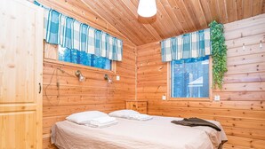 Ein Holzhüttenraum mit einem Bett, zwei Vorhängen und einem kleinen Tisch, sowie einer hängenden Pflanze.
