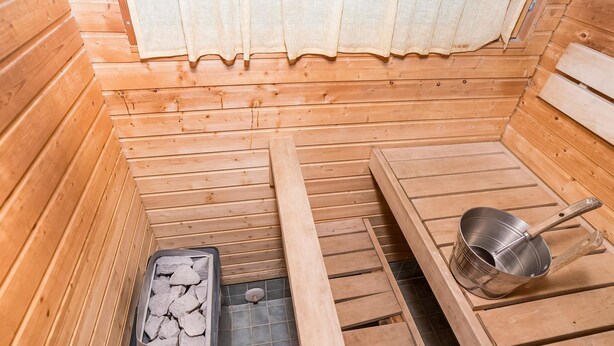 Eine Holzsauna mit einer Sitzbank, einem steinbegehnen Behälter und einem Metall-Eimer.