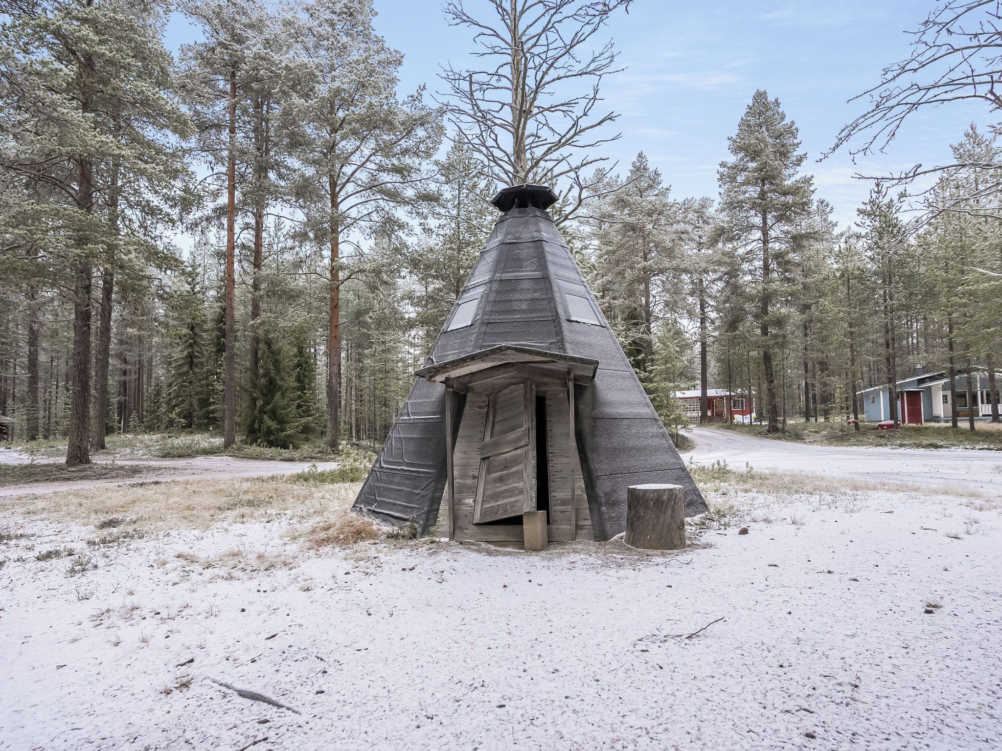 Et snedækket kegleformet bygning i et skovområde med klar himmel.
