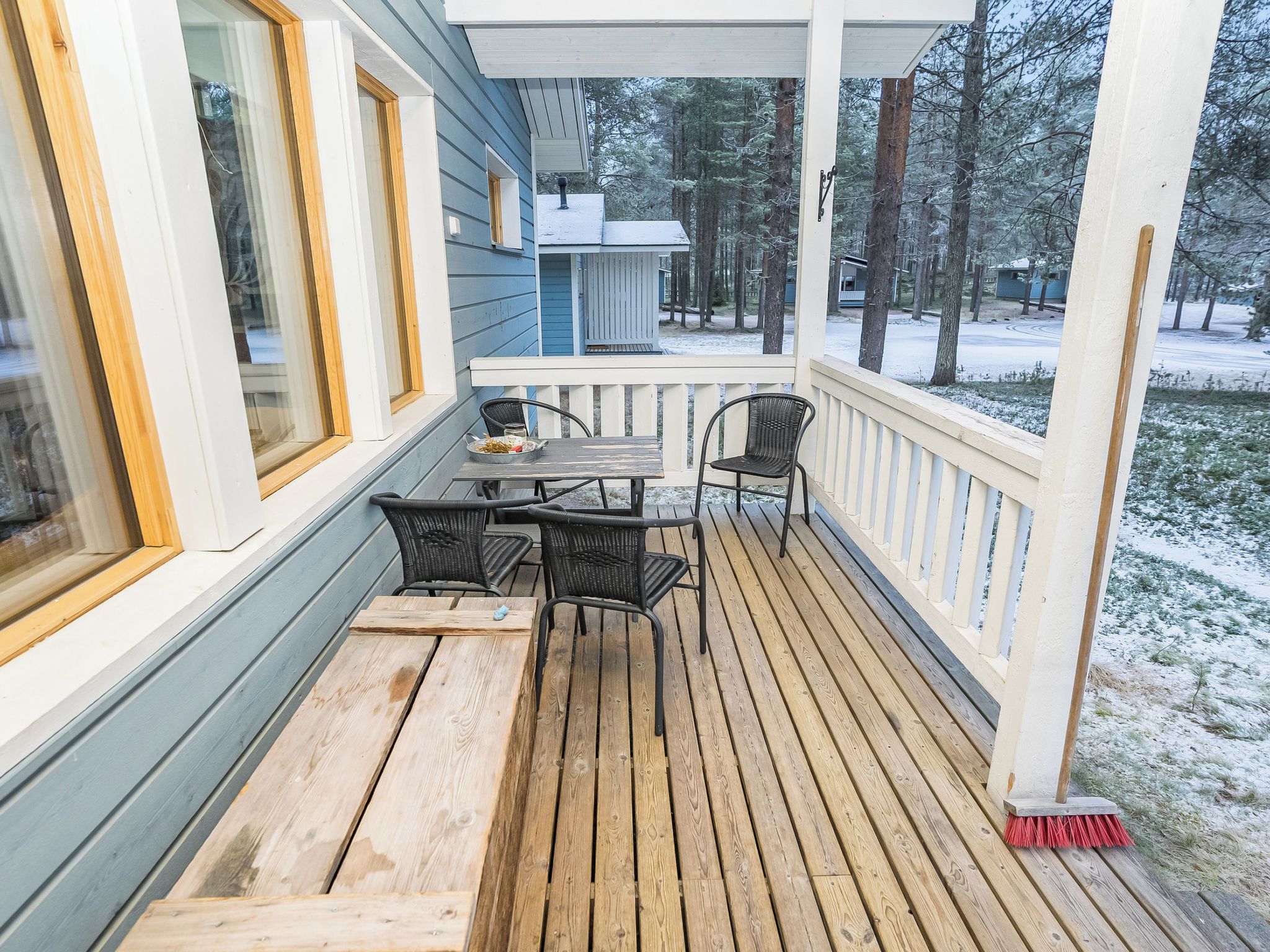 A wooden deck with a table and chairs, overlooking a snowy landscape with trees.