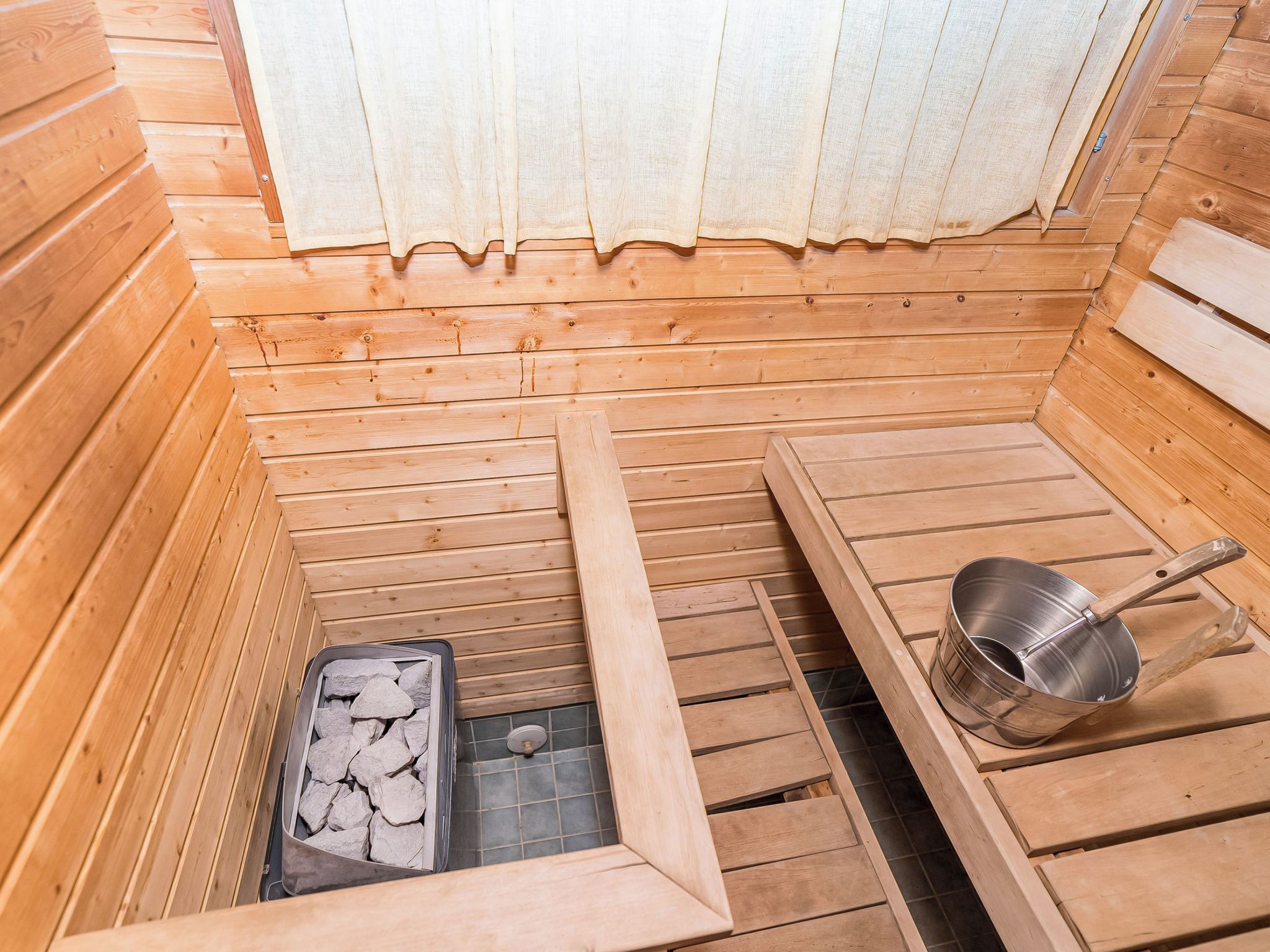 Een sauna met houten banken, een metalen wasbak en een bak met stenen.