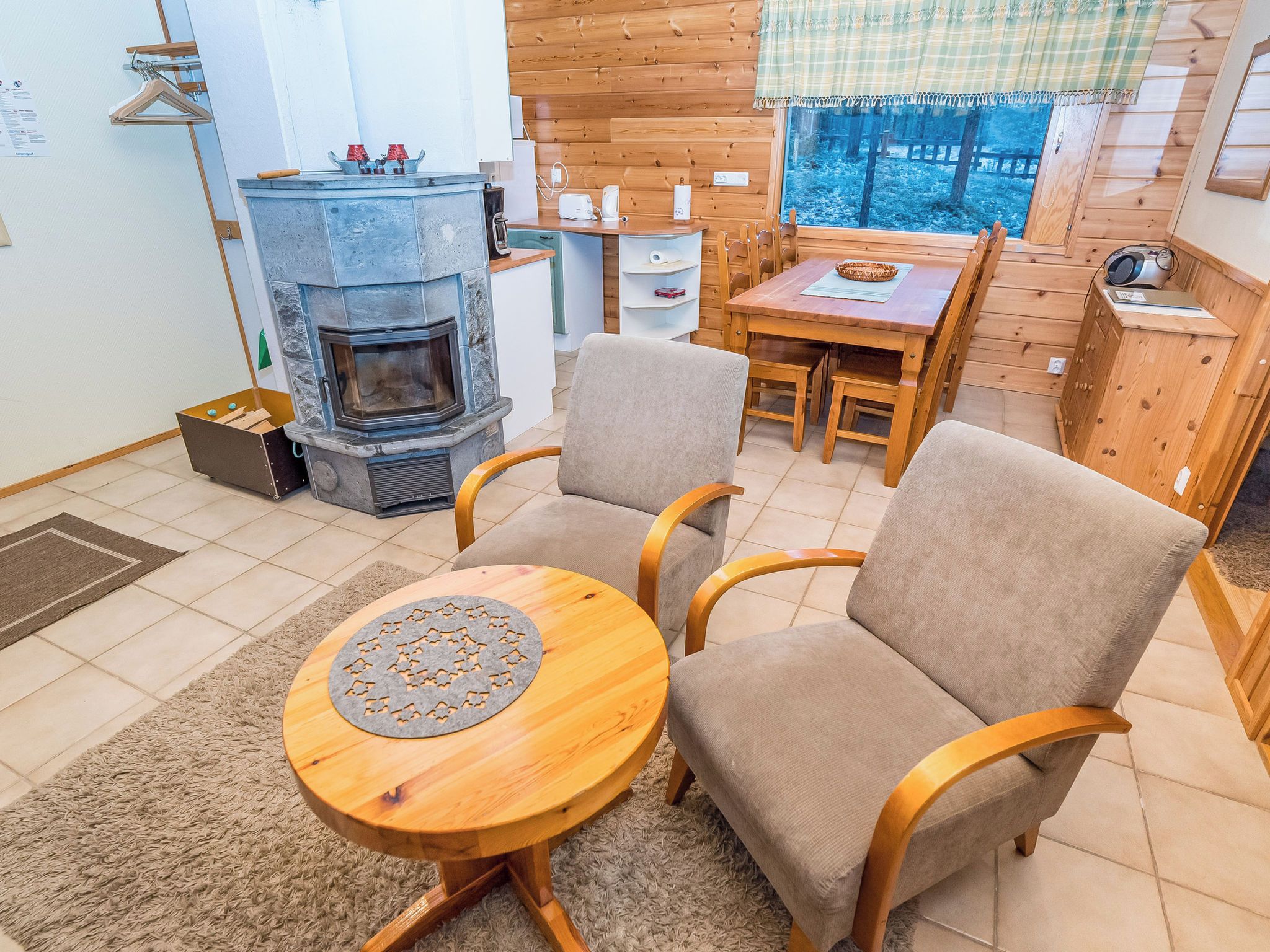 Een gezellige woonkamer met een stenen openhaard, twee fauteuils, een houten salontafel en een eettafel met stoelen.