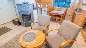 Een gezellige woonkamer met een stenen openhaard, twee fauteuils, een houten salontafel en een eettafel met stoelen.