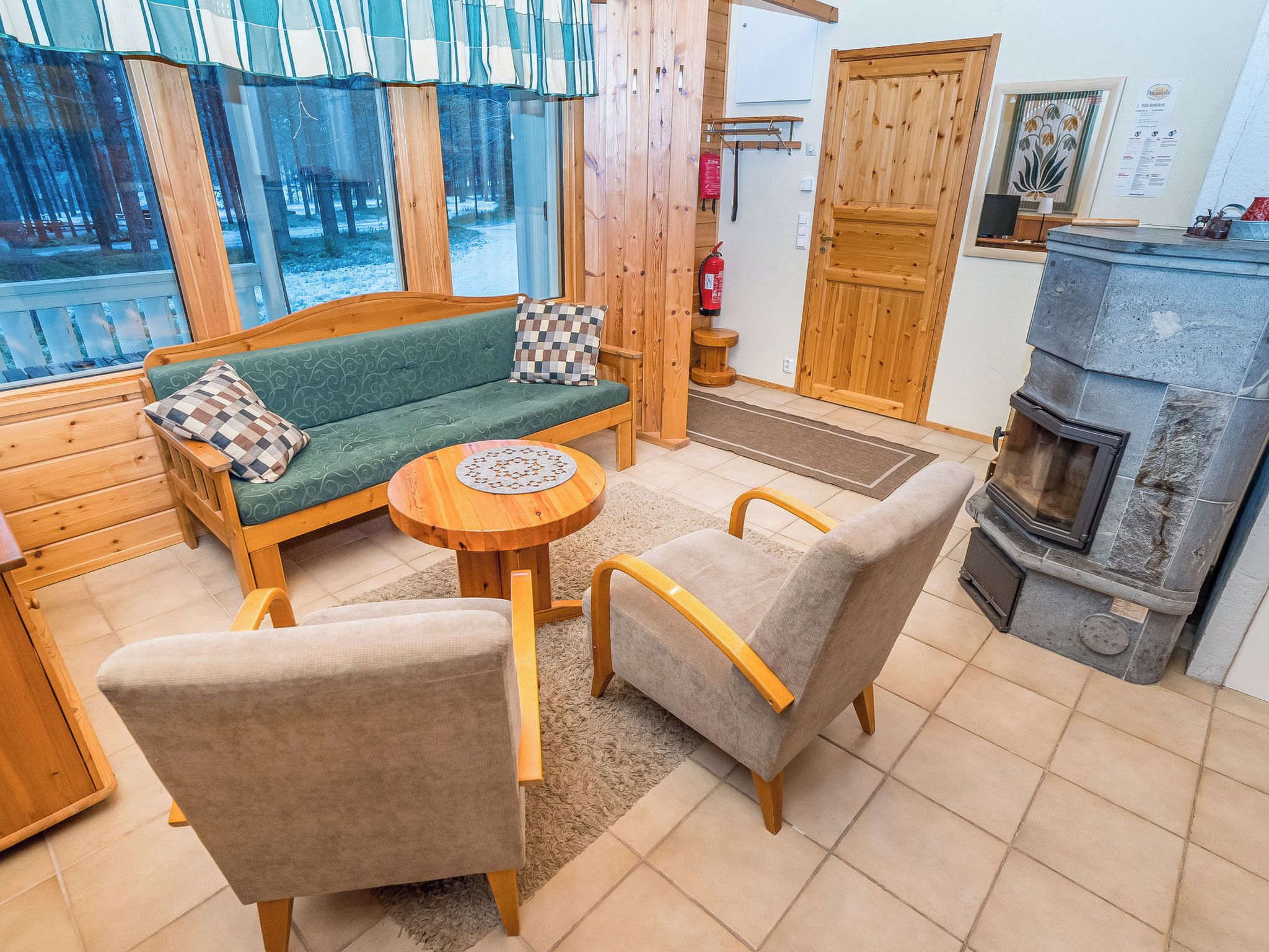 A cozy cabin interior with a sofa, chairs, a round wooden table, a fireplace, and a window overlooking a snowy landscape.