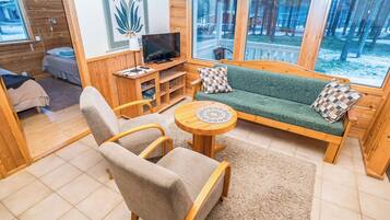 A cozy cabin interior with a sofa, armchair, and a television on a wooden stand.