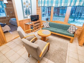A cozy cabin interior with a sofa, armchair, and a television on a wooden stand.