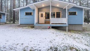 Eine zweistöckige Holzhütte mit Veranda, umgeben von einem Wald.