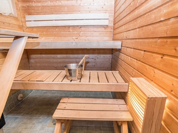 A sauna with wooden benches and a metal bucket.