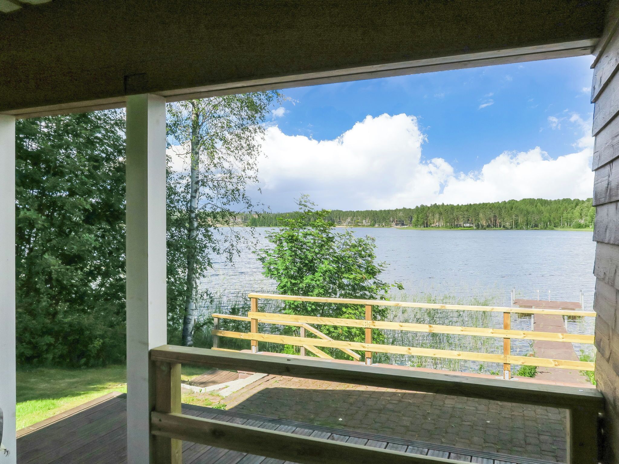 A view from a window with a wooden deck and a lake.